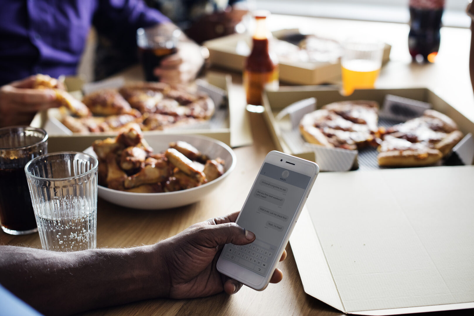 Person texting on phone while eating pizza with friends